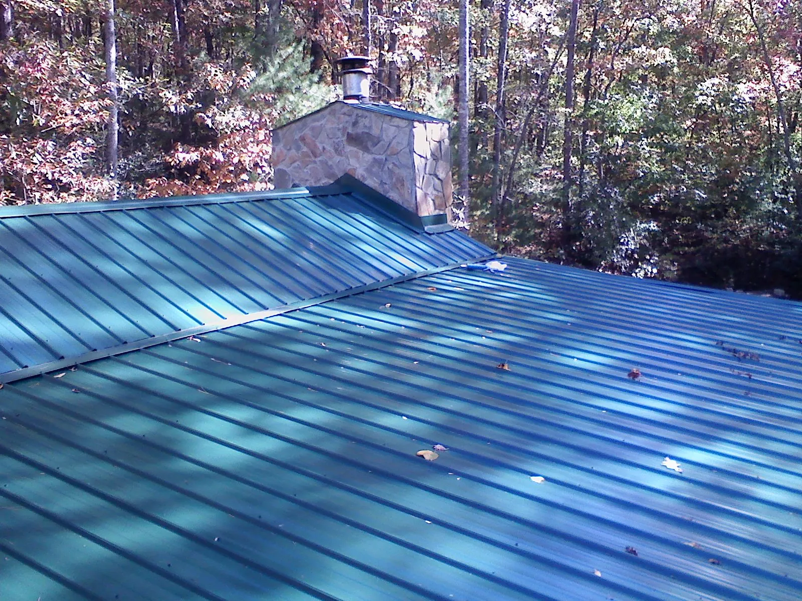 New green metal roof and stone chimney surrounded by autumn woods in Concord