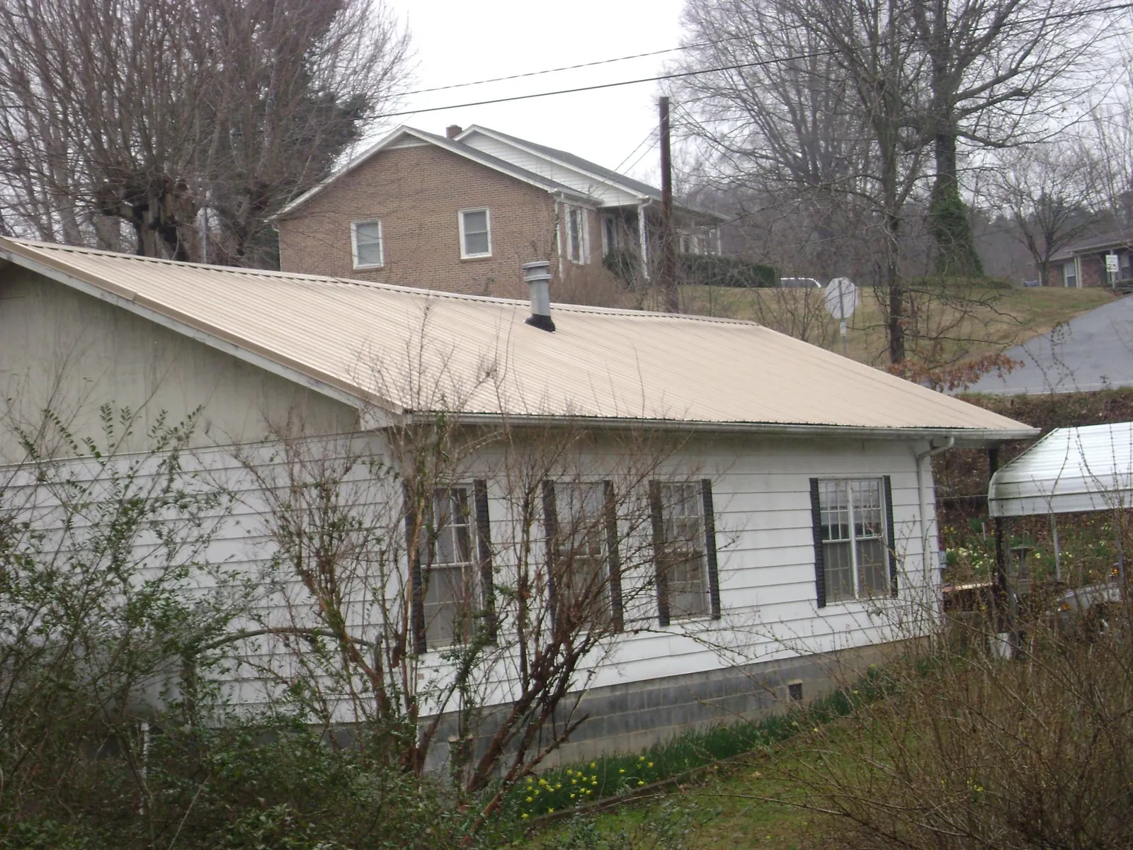 Tan metal roof on a white sided house set into a hillside — Commercial Roofing by Roofing Brothers in Concord